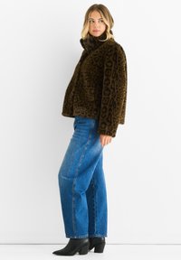 Giacca in pelliccia sintetica maculata marrone con colletto alto, indossata con jeans blu a vita alta e stivali neri con tacco alla caviglia.