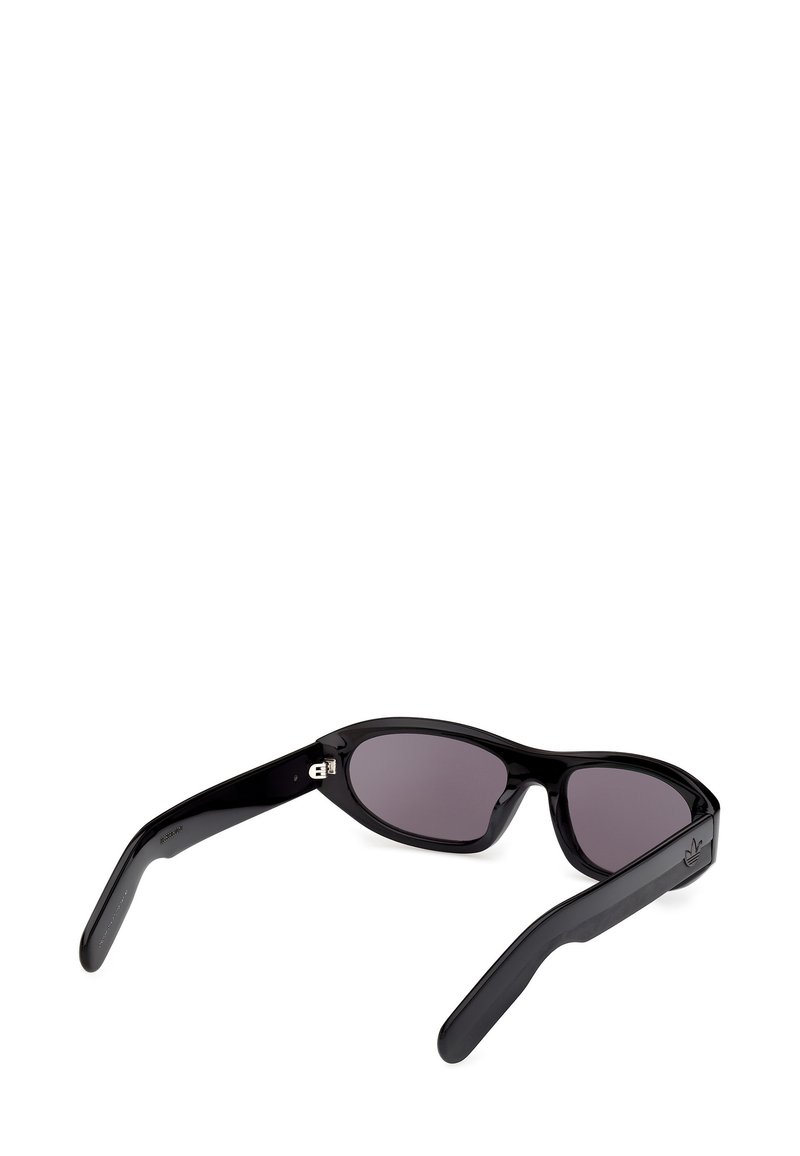 Schwarze rechteckige Sonnenbrille mit dunkel getönten Gläsern und dicken, glänzenden Bügeln, die auf einer weißen Fläche liegen.