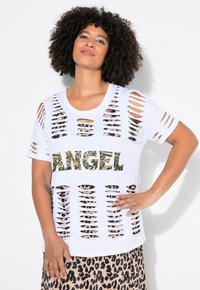 Valkoinen T-paita, jossa on suuri leikkauskuvio ja sanan "ANGEL" leopardikuvio. Löysä malli, jossa on lyhyet hihat, kerrostettuna leopardikuvioisen hameen päälle.