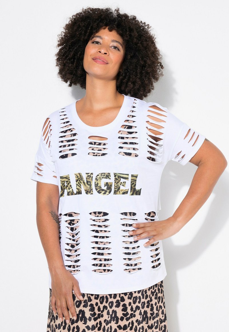 Valkoinen T-paita, jossa on suuri leikkauskuvio ja sanan "ANGEL" leopardikuvio. Löysä malli, jossa on lyhyet hihat, kerrostettuna leopardikuvioisen hameen päälle.