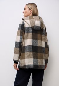 Fleecová bundy s kapucí a velkým kostkovaným vzorem v odstínech hnědé, šedé a krémové. Má volný střih a dlouhé rukávy.