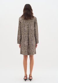 Leopardmönstrad klänning i tyg, med långa ärmar, rak passform och mitt bak på klänningen. Avslutningen inkluderar minimalistiska svarta skor.