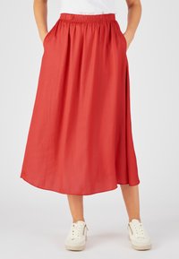Falda roja, hasta la rodilla, hecha de una tela ligera con una cintura elástica y bolsillos laterales, combinada con zapatillas blancas.