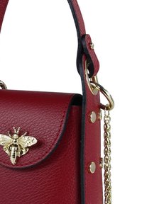 Sac à bandoulière en cuir rouge avec une finition texturée, emblème d'abeille doré, bandoulière en chaîne et accents noirs le long des bords et des ferrures.