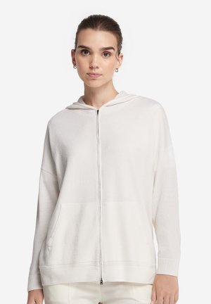 Biała bluza z kapturem na zamek, wykonana z miękkiego materiału, o luźnym kroju, z kieszeniami z przodu i ściągaczami na rękawach.