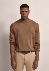 Brauner strukturierten Pullover mit Rundhalsausschnitt und langen Ärmeln, kombiniert mit hellbeigen Hosen und einem braunen Gürtel. Einfaches, monochromatisches Design.