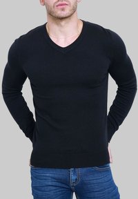 Pull noir en V ajusté, fabriqué en tissu tricot lisse. Présente des manches longues et un ourlet côtelé, associé à un jean bleu.