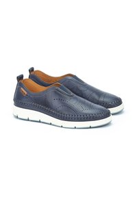 Zapatos de piel azul marino sin cordones con diseño perforado, acentos de costura y suela de goma blanca. Forro interior marrón con lazada en el talón.