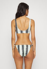 Conjunto de biquíni com uma base verde menta e padrões abstratos em preto e branco. O top possui alças largas; a parte de baixo apresenta um detalhe de amarração lateral.