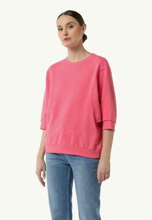 Różowy oversize'owy sweter z okrągłym dekoltem, opadającymi ramionami i ściągaczami. W połączeniu z jasnoniebieskimi dżinsami. Gładki tekstur materiału.