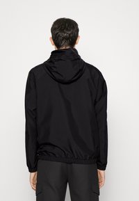 Black lightweight jacket with a hood, elastic cuffs, and waistband; smooth texture and minimal design, suitable for casual or outdoor wear.