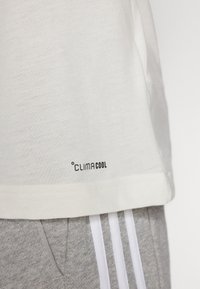 Hvid bomulds T-shirt med et ClimaCool mærke ved kanten, parret med grå sweatpants med hvide striber langs siderne.