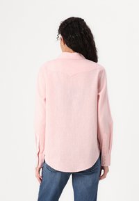 Camisa de manga longa rosa com uma textura subtil, gola colarinho e barra arredondada. Apresenta costuras de yoke na frente e nas costas e punhos com botão.