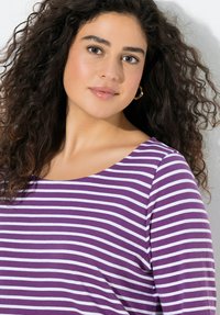 Lila-weiß gestreiftes Langarmoberteil mit rundem Ausschnitt. Der Stoff wirkt weich und dehnbar, mit einer lockeren Passform.