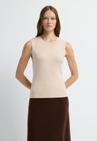 Beige mouwloos topje van zachte gebreide stof, met een ronde halslijn en een aansluitende pasvorm, gecombineerd met een bruine gestructureerde rok.