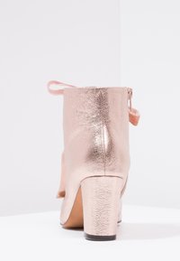 Stivaletto alla caviglia metallizzato rosa lucido con tacco a blocco e cerniera posteriore, esposto su uno sfondo bianco semplice.