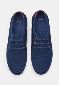 Tengerés kék hálós sneakers, texturált felülettel, öt fűzőlyukkal, piros díszítéssel a szegélyen és fehér gumitalppal.