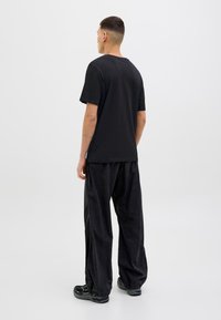 Sort bomulds t-shirt med rund halsudskæring, parret med løse sorte bukser. Stofmaterialet ser blødt ud med en glat tekstur.