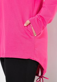 T-shirt rose à manches longues avec une poche latérale, un ourlet courbé et un cordon ajustable en bas. Matière en coton doux pour le confort.