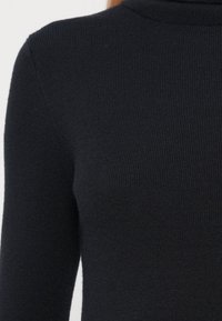 Suéter negro de punto acanalado con cuello alto y mangas largas. La tela es suave y tiene una textura lisa.