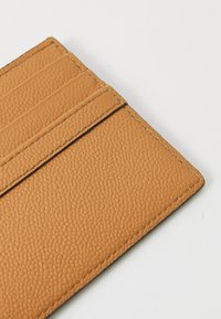 Tan leather cardholder featuring a textured surface, four card slots, and visible stitching along the edges.