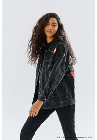 Czarna dżinsowa kurtka o luźnym kroju, z zapięciem na guziki, bocznymi kieszeniami i różową okrągłą naszywką na lewym ramieniu.