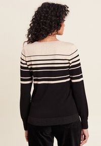 Schwarzer und goldgestreifter Pullover mit langen Ärmeln; verfügt über horizontale metallische Streifen und einen taillierten Saum. Weiche, gestrickte Stoffstruktur.