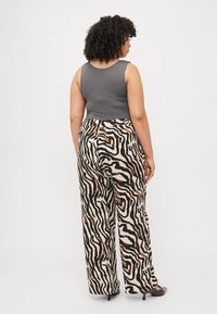 Gray sleeveless top paired with high-waisted, wide-leg trousers featuring a zebra stripe print in black, beige, and brown tones.