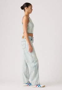 Μπλε κροπ τοπ από τζιν και τζιν παντελόνι ψηλόμεσο με φαρδιά μπατζάκια. Εμβληματικό δερμάτινο ταμπελάκι στο πίσω μέρος. Αθλητικά παπούτσια με κόκκινες, μπλε και λευκές λεπτομ έρειες.