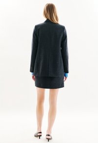 Blazer de cuadro navy con una única abertura, combinado con una minifalda a juego. Presenta un corte entallado y una textura sofisticada.