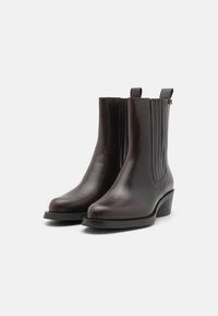 Bottines en cuir marron avec bout arrondi, panneaux latéraux élastiques et petit talon carré. Design minimaliste et texture lisse.