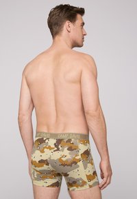 Camo-patterned boxer briefs in earth tones of brown, green, and beige, featuring a branded elastic waistband and a snug fit.
