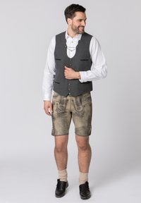 Grau gestrickte Weste mit grünen Akzenten, kombiniert mit strukturierten beigen Lederhosen, die mit aufwendiger Stickerei und dekorativen Knöpfen versehen sind. Schwarze Schuhe und knielange Socken.