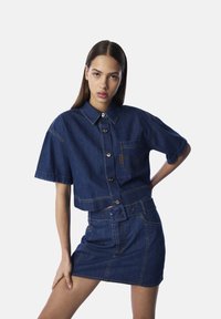 Chemise en denim courte avec boutonnage à l'avant et manches courtes, accompagnée d'une minijupe en denim assortie, dotée d'une taille ceinturée et de poches.