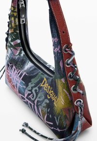 Mitmevärviline käekott, millel on graffiti-stiilis mustrid, tõmblukuga sulgur ja tekstureeritud rihm. Omab silmadega aktsente ja punutud külgedetaili.