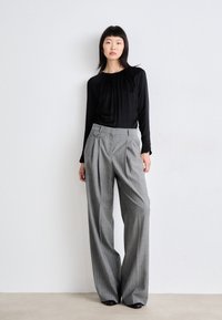 Mustapaitainen pitkähiha blouse, jossa on kerrottu kaula-aukko, yhdistettynä korkeavyötäröisiin harmaisiin raidallisiin housuihin, joissa on sivu-nappi yksityiskohta.