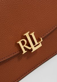 Brązowa skórzana torebka charakterystyczna za teksturowaną powierzchnię, z klapką i wyraźnym złotym akcentem w postaci logo "RLL".