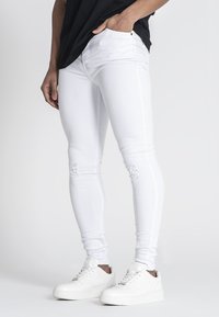 Jeans ajustados blancos con detalles desgastados en las rodillas, elaborados en denim. Combinados con zapatillas blancas, que presentan una textura sutil y un corte slim.