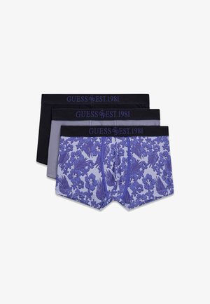 Drei Herren-Boxershorts gestapelt; eine mit floralen Mustern in Lilatönen, eine einfarbig grau und eine einfarbig schwarz, alle mit schwarzen Bunds, auf denen "GUESS EST. 1981" steht.