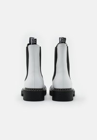 Botines en blanco y negro con cuero suave y paneles laterales elásticos, que cuentan con costuras en contraste, suelas gruesas y lengüetas para tirar.