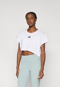 Άσπρο cropped t-shirt με μαύρο λογότυπο Adidas, κοντά μανίκια, συνδυασμένο με ανοιχτό μπλε ψηλόμεσα κολάν. Ομαλό ύφασμα, μίνιμαλ σχέδιο.