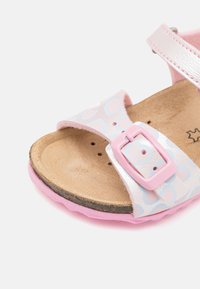 Ροζ σανδάλια με γυαλιστερή, υφή συνθετικού υλικού που διαθέτει σχέδιο καρδιάς, ρυθμιζόμενη αλυσίδα και μαλακή σόλα.