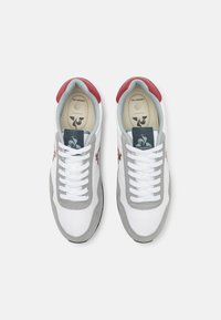 Baskets blanches avec des accents en suède gris et un onglet de talon rouge. Elles disposent de lacets blancs, d'un col rembourré et d'une semelle intérieure marquée avec un logo.