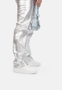 Un pantalon argent métallisé avec une finition brillante, associé à des baskets blanches et un petit sac à main bleu clair. Coutures détaillées sur le pantalon.