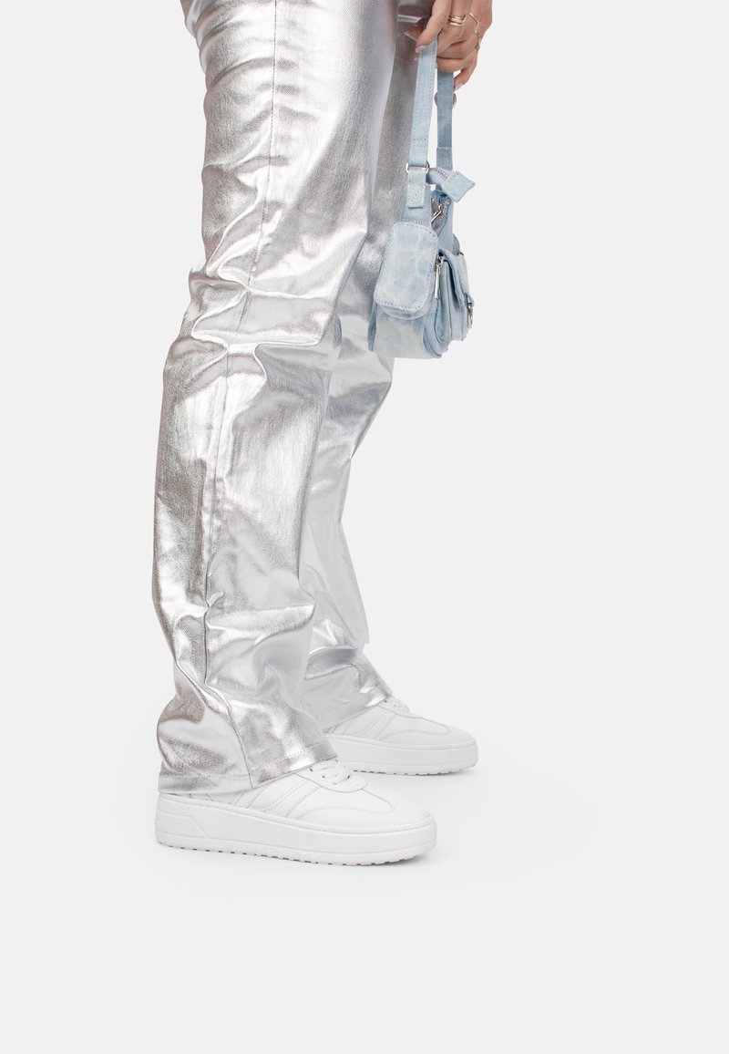 Un pantalon argent métallisé avec une finition brillante, associé à des baskets blanches et un petit sac à main bleu clair. Coutures détaillées sur le pantalon.