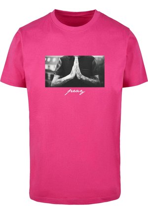 T-shirt en coton rose avec un graphisme noir et blanc représentant des mains en position de prière, avec le mot "prier" imprimé en dessous en police blanche.