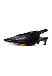 Zapatos de tacón negro de piel con puntera afilada y tirantes traseros, que cuentan con un tacón delgado y un llamativo detalle en forma de hebilla circular plateada, presentando una textura suave y un diseño minimalista.
