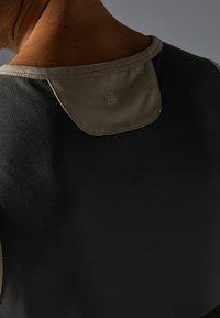 Sort atletisk tanktop med struktureret stof og en kontrastfarvet tan krave. Har et lille logo på ryggen nær nakken.