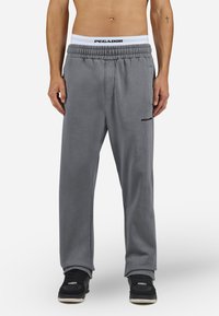 Pantaloni de trening gri cu o croială relaxată, talie elastică cu logo-ul "PEGADOR" și buzunare laterale. Purtați cu pantofi sport negri.
