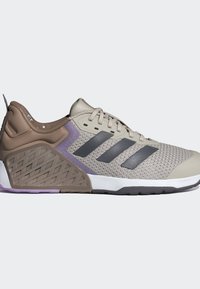 Ljusbeige sportskor med en texturerad mesh-överdela, grå accentfärger och lila detaljer på hälen och sulan. Har de karakteristiska tre ränderna.